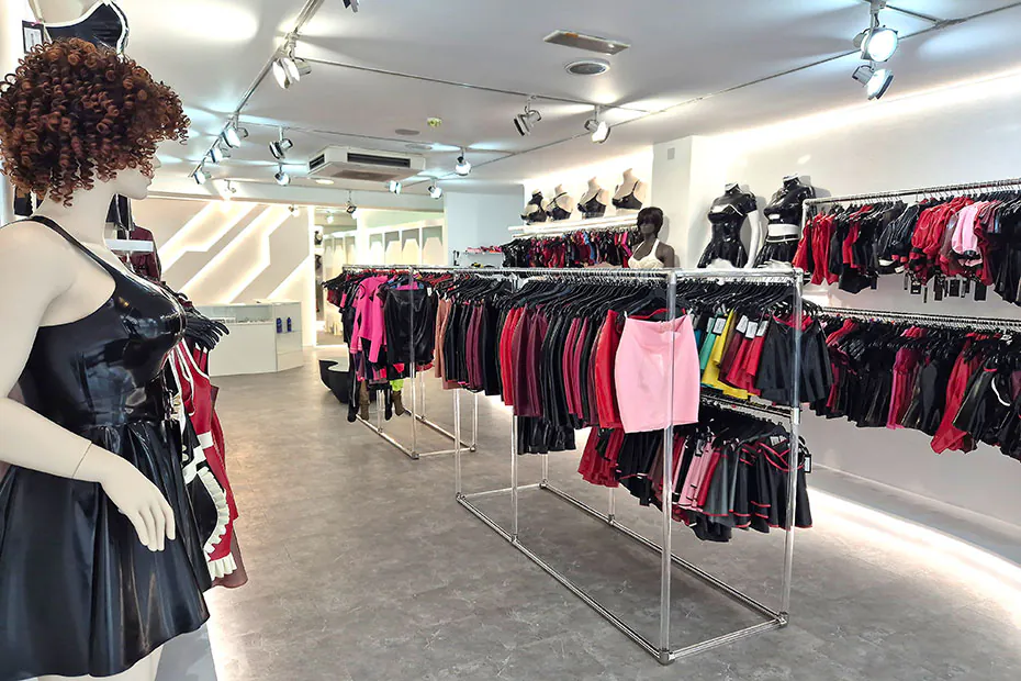 A mannequin in a black latex dress beside chrome rails of pink, red and black latex garments.